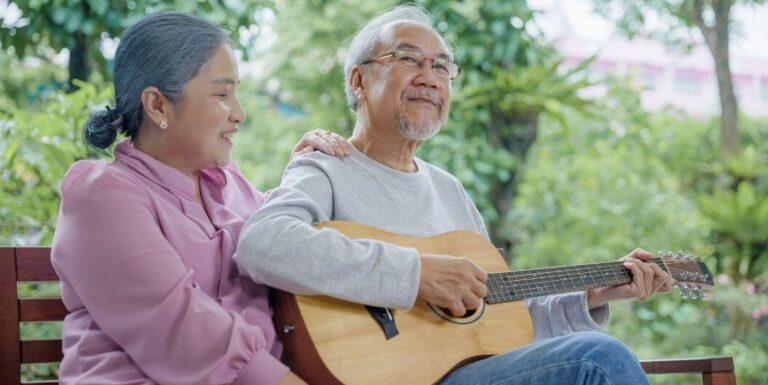 Elderly Couple Playing Guitar on Bench at Assisted Living Facility