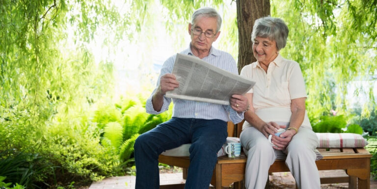 Elderly Couple Reading Newspaper Outdoors at Assisted Living Facility